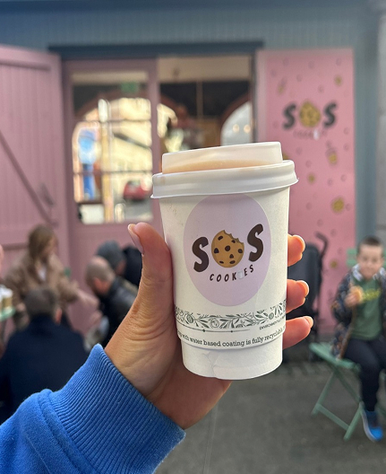 Hand holding SOS coffee cup in front of pink shop wall